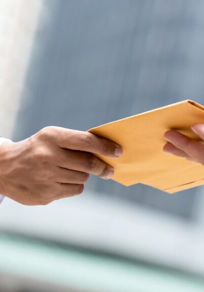Close up portrait of  businessman hand recieving yellow envelope from boss in urban city background